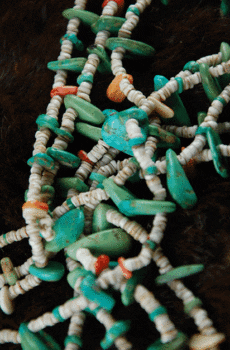 Close-up of a Wrapped Three Strand Bird Fetish Necklace with turquoise stones and white beads on a dark furry background.