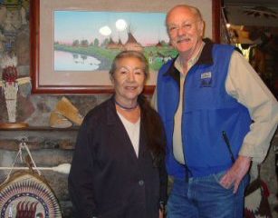 An elderly couple standing in a room decorated with Native American art and crafts, smiling at the camera.