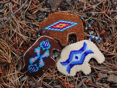 Three beadwork pieces with indigenous designs lying on a bed of pine needles.