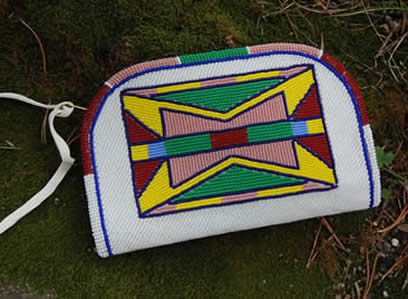 A colorful beaded bag with geometric patterns, placed on a grassy surface.
