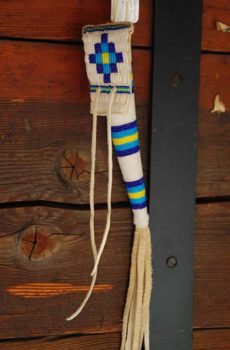 A traditional Native American beaded bag hanging against a wooden wall, featuring white fringes and colorful bead patterns.