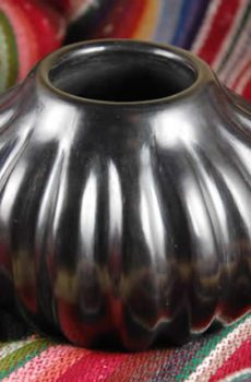 A shiny, ribbed silver vase sits on a colorful woven fabric with red, yellow, and green stripes.