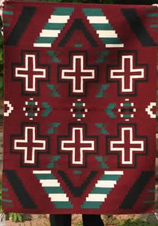 A Revival rug featuring symmetrical geometric designs in red, black, white, and turquoise, displayed vertically.