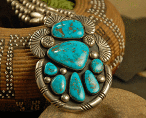 A close-up of a turquoise and silver American Indian Art jewelry piece displayed on a textured fabric background.