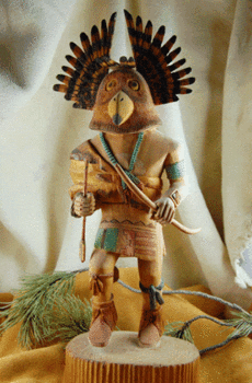 Wooden carving of a Owl Kachina doll, depicted with detailed feather headdress and traditional attire, holding a bow, standing on a round base.