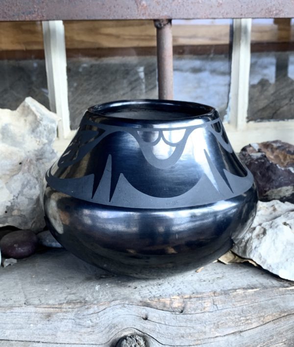 A black vase sitting on top of a cement floor.
