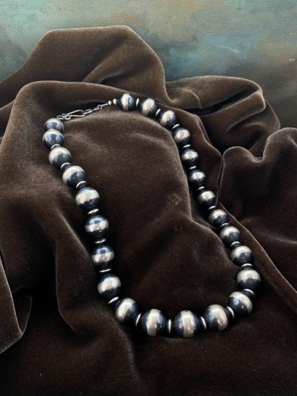 A necklace of silver and black beads on top of brown fabric.