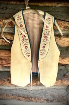 A vest hanging on the wall of a log cabin.