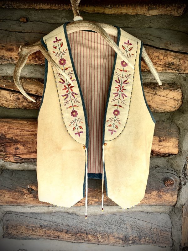 A vest hanging on the wall of a log cabin.