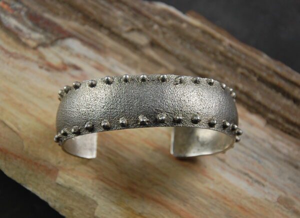 A silver bracelet with some metal rivets on it
