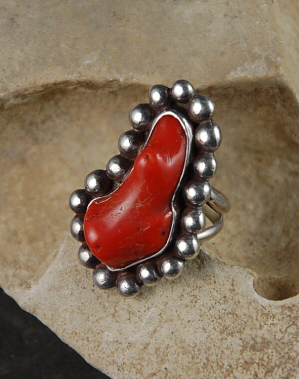 A red coral ring is shown on top of a rock.