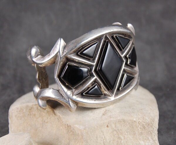 A silver ring with black stones on top of a rock.