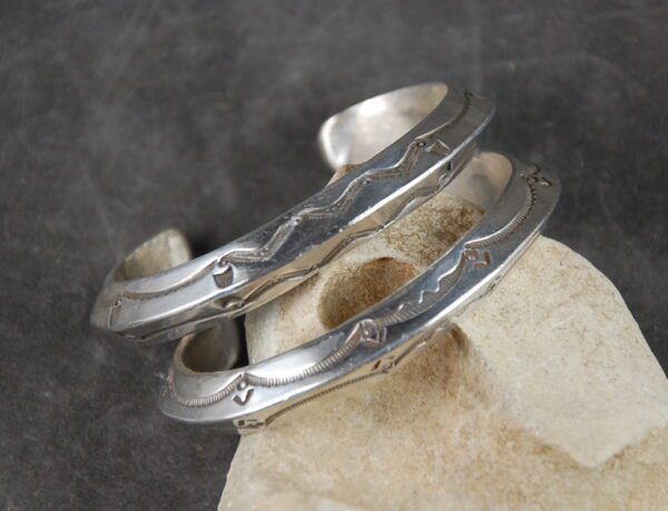 A pair of silver bracelets sitting on top of a stone.