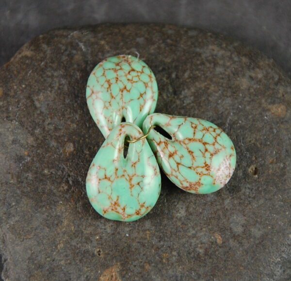 Three green and brown speckled beads sitting on a rock.