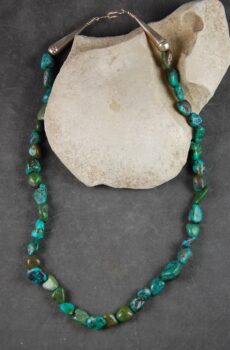A necklace of turquoise is sitting on the rock.