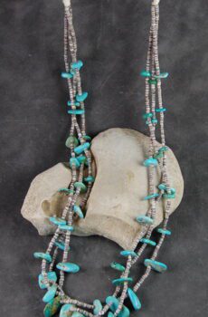 A necklace of turquoise and silver beads on a gray background.