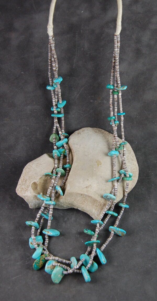 A necklace of turquoise and silver beads on a gray background.