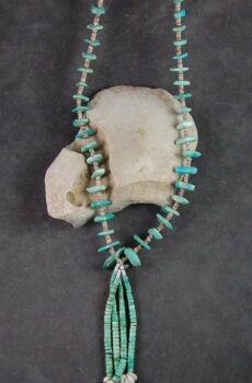 A necklace of turquoise and white beads on a stone slab.
