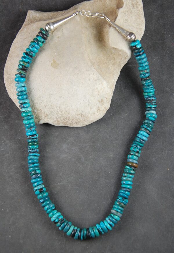 A necklace of turquoise beads is sitting on the beach.